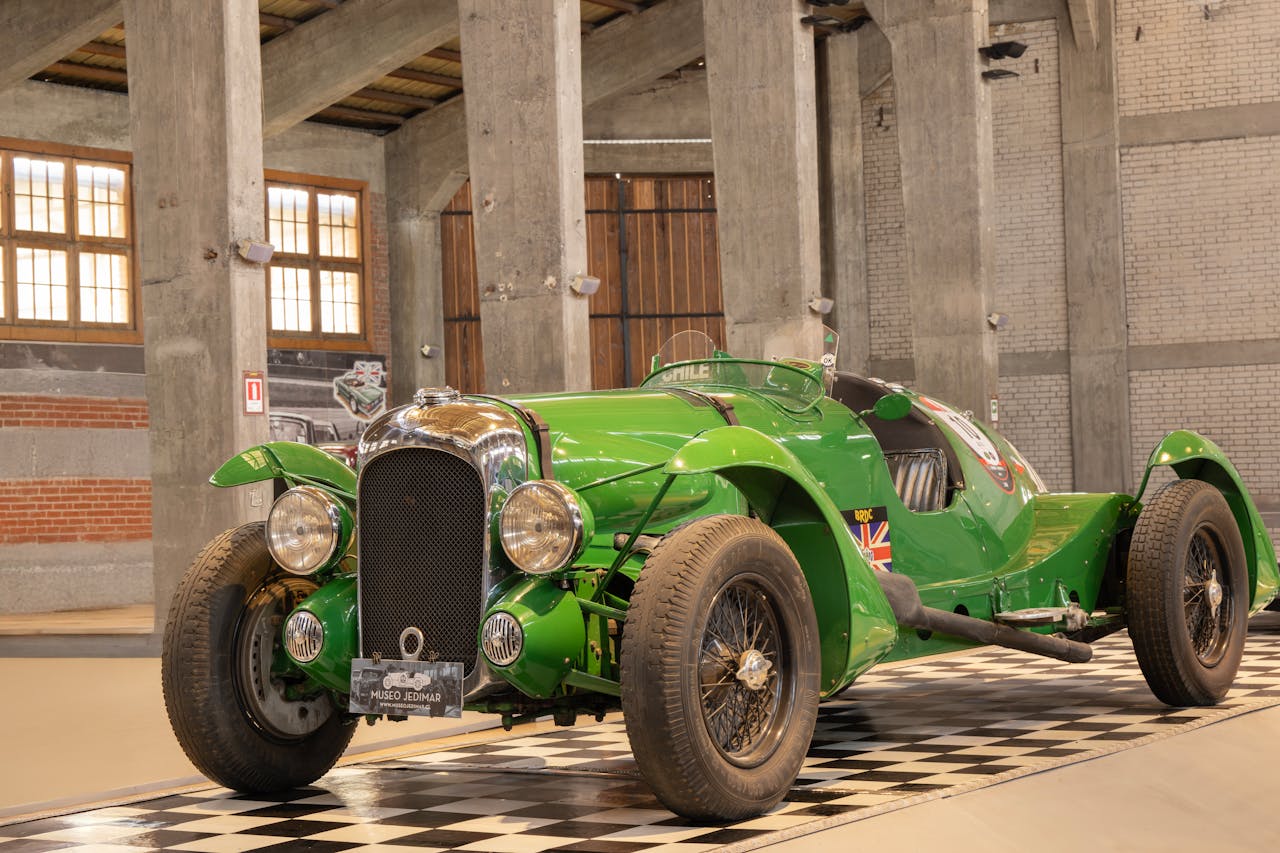 A stunning green vintage car displayed indoors in a rustic, industrial building.